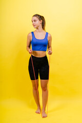 Portrait of gentle muscular woman holding skipping rope on her neck isolated over yellow background