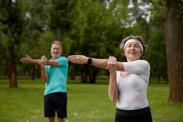Senior couple doing warm-up exercises during physical therapy class on nature