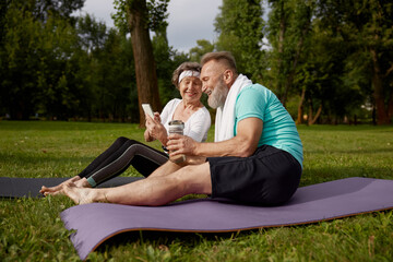 Senior couple sitting on fitness mats rest after yoga training in park