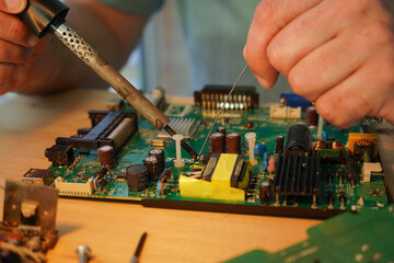 A man holds a soldering iron in his hand and solders a microcircuit