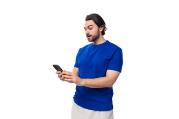 young caucasian brunette man with a beard in a blue t-shirt texting on a mobile phone