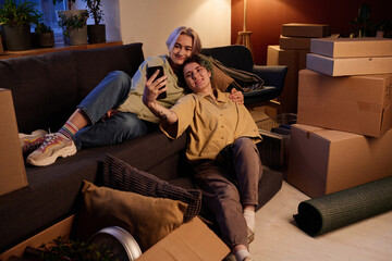 Friends resting on sofa and watching video on smartphone, they resting after move in new apartment
