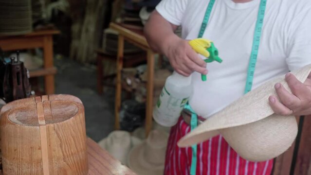 An adult Hispanic man is spraying water to shape a natural fiber hat. Concept of handmade traditional clothing
