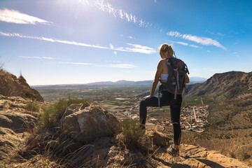 Hiker with backpack standing on top of the mountain and enjoying valley view at sunrise