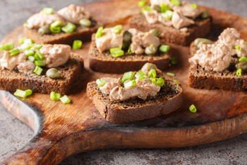 Tasty sandwiches with cod liver, capers and green onion close-up on a wooden board on the table. Horizontal