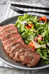 Beef tagliata with arugula, parmesan and cherry tomatoes is a delicious main course made with beef entrecote close-up on a plate on the table. Vertical