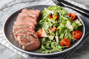 Traditional Italian main dish Beef tagliata tender steak, arugula, cherry tomatoes, Grana Padano shavings, balsamic reduction close-up on a plate on the table. Horizontal