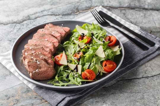 Beef steak tagliata with arugula, parmesan,  cherry tomatoes and balsamic close-up on a plate on the table. Horizontal