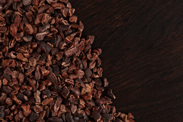 Unsweetened Organic Cacao Nibs on brown wooden surface, top view. Crunchy pieces of peeled, crushed...