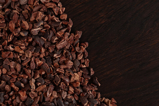 Unsweetened Organic Cacao Nibs on brown wooden surface, top view. Crunchy pieces of peeled, crushed and lightly roasted cocoa beans. Natural Sugar-free product