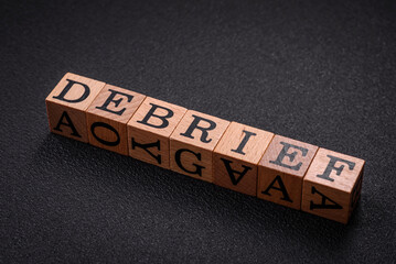 The inscription debrief in wooden cubes on a dark concrete background