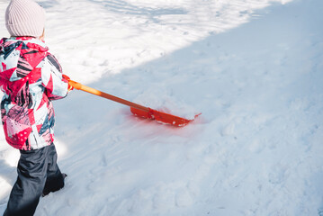 Child cleaning snow with a shovel in the backyard or countryside. Hello winter