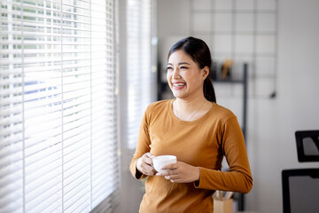 Portrait of a smiling asian businesswoman standingin home office and cup of coffee in hand .