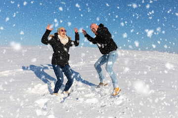 Ein verliebtes Paar bestehend aus Mann und Frau springen voller Freude im Schnee in die Luft und...