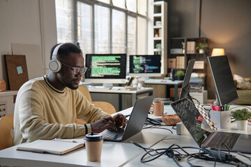 Software developer listening to music in headphone when coding on laptop in office of IT company