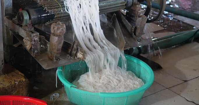 Rice noodles are cut to the desired length and fall into a plastic basket.