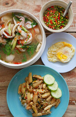 On top of the table background, there is a lunch set with fried eggs, Tom Yam Kung, lemon grass soup, and basil-fried crab and prawn. Thailand street cuisine idea.