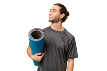 Young sport man going to yoga classes while holding a mat over isolated background looking to the side and smiling