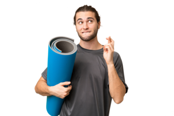 Young sport man going to yoga classes while holding a mat over isolated background with fingers crossing and wishing the best