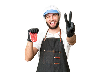 Butcher man wearing an apron and serving fresh cut meat over isolated chroma key background smiling and showing victory sign