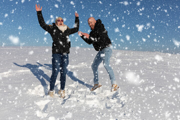 Ein verliebtes Paar bestehend aus Mann und Frau springen voller Freude im Schnee in die Luft und zeigen ihre Freude durchs Lachen und Lächeln - obrazy, fototapety, plakaty