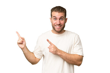 Young handsome caucasian man isolated on green chroma background frightened and pointing to the side