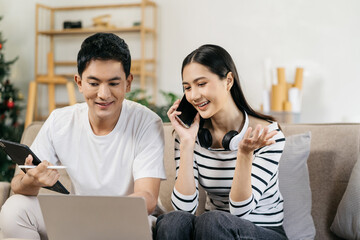 Young couple sitting on couch are using credit card payment through smartphone, buying furniture...