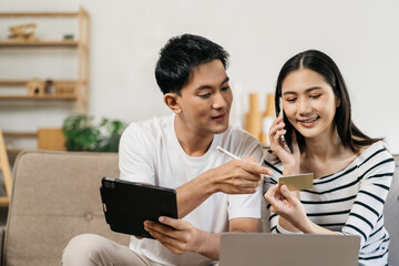 Young couple sitting on couch are using credit card payment through smartphone, buying furniture enter house, working on design together having conversation.