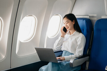 Young Asian executive excels in first class, multitasking with digital tablet, laptop and...