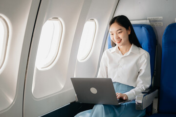 Young Asian executive excels in first class, multitasking with digital tablet, laptop and...
