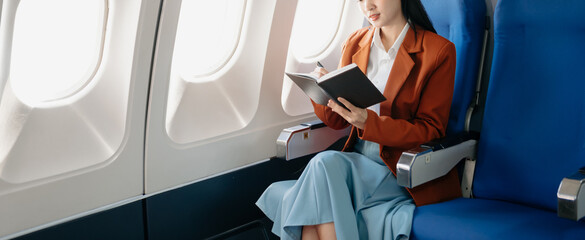 Attractive Asian female passenger of airplane sitting in comfortable seat while working laptop and tablet with mock up area using wireless connection.