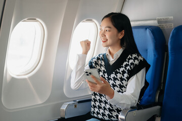 Fototapeta premium Attractive Asian female passenger of airplane sitting in comfortable seat while working laptop and tablet with mock up area using wireless connection.