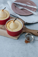 two pear soufflés in red bowls stand on a wooden board, next to a plate with a vintage fork and knife and a towel. strainer with cinnamon