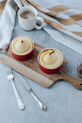 two pear soufflés in red bowls stand on a wooden board, next to a white cup of coffee, a vintage fork with a knife and a towel