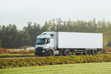 Front view of the European truck vehicle on a motorway with dramatic sunset light. Concept of cargo transportation and supply. Loaded European truck on motorway in beautiful sunset light.