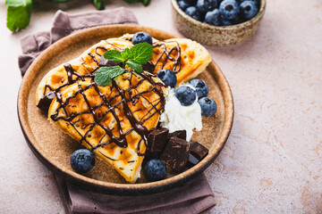 Homemade waffles with blueberries, chocolate sauce and cream cheese in a plate and a beige...