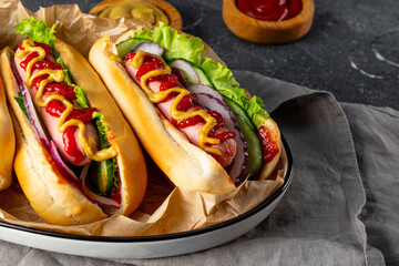 Homemade hot dogs with sausage, green salad, cucumber and red onion on the grey background close up