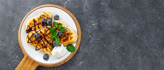 Homemade waffles with blueberries, chocolate sauce and cream cheese in a plate and a grey background top view web banner copy space for text