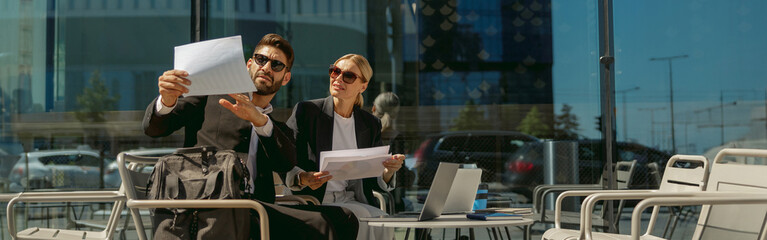 Two business partners working with documents sitting outside of office on cafe terrace