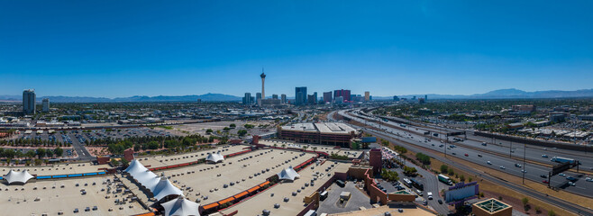 Panoramic Las Vegas cityscape with Stratosphere Tower, surrounded by mountains, showcasing a bustling mix of modern and historic architecture under a clear blue sky.