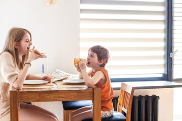 Children eating pizza at stylish home interior. Teen girl and little boy biting slice of pizza....