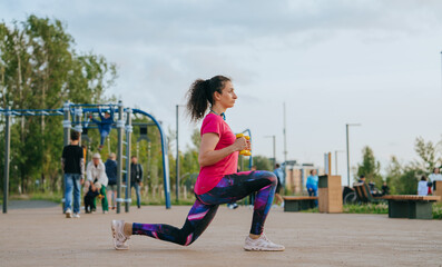 professional female athlete trains on the playground with dumbbells, makes lunges and trains her...