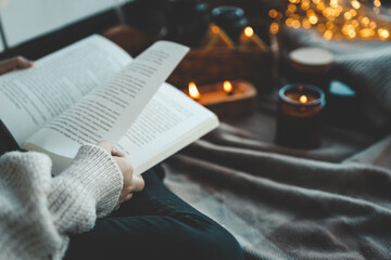 Girl with a book in her hands in a cozy home atmosphere - obrazy, fototapety, plakaty