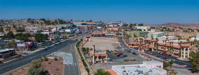 Poster Aerial view of a Barstow U.S. town nestled in a desert valley, featuring beige and brown buildings with terracotta roofs, palm trees, and a grid-like street layout. © ingusk