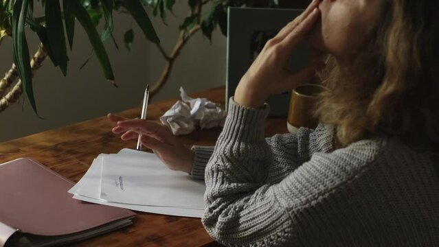 Pensive female writer writing book in home office. Writer's block.