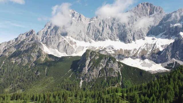 4K drone shot of majestic Dachstein Glacier, Styria, Austria in the Alps. Popular area for Alpine and cross-country skiing, snowboarding. Huge rock formations overlook lush green fields.