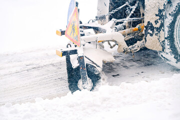 Tractor with rotating brush sweeps snow from snowy sidewalk during snowfall. Snow removal work,...