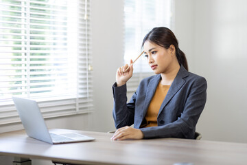 Portrait of young Business asian woman using computer at home sitting in the office working and studying alone. Thoughtful serious woman thinking on new projects.