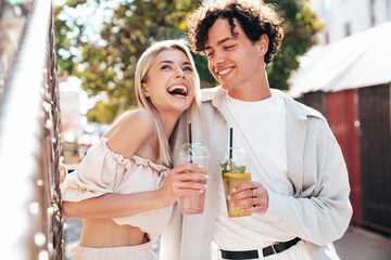 Young smiling beautiful woman and her handsome boyfriend in casual summer clothes. Happy cheerful family. Female having fun. Couple posing in street. Holding and drinking cocktail drink in plastic cup