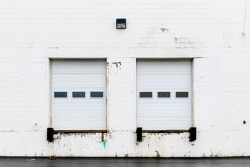 Fototapeta premium Front view of a truck loading bay with rubber bumpers in the white concrete wall of a warehouse with a closed white roller shutter door